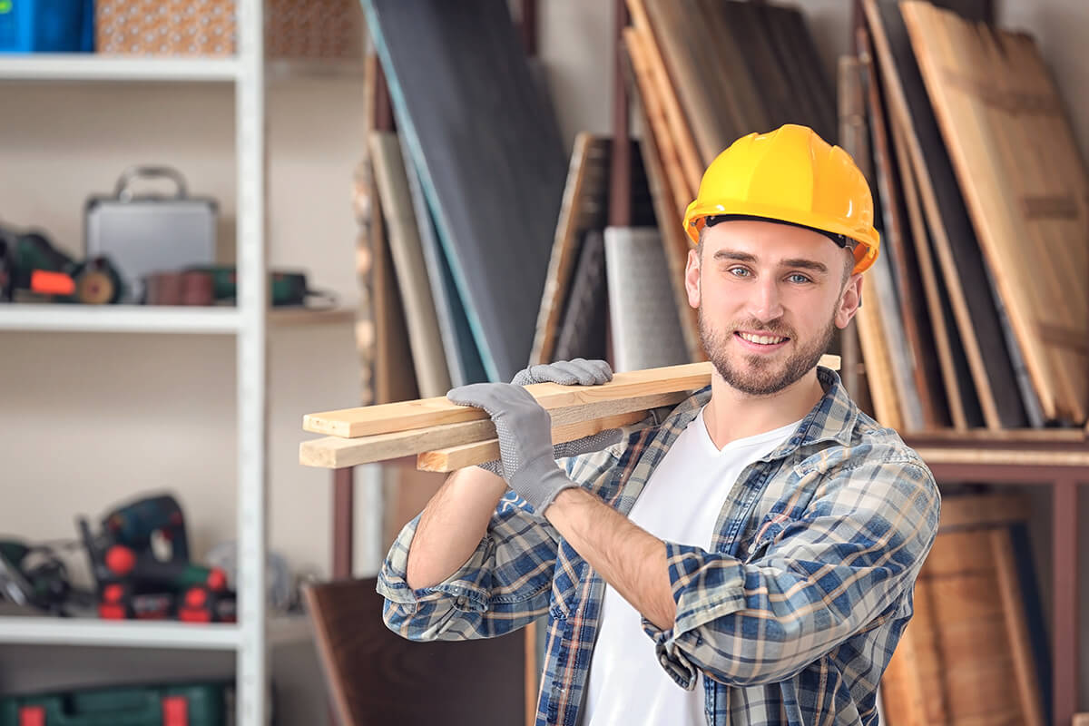 Un homme de la construction avec madrier sur l'épaule avec un casque de protection jaune.